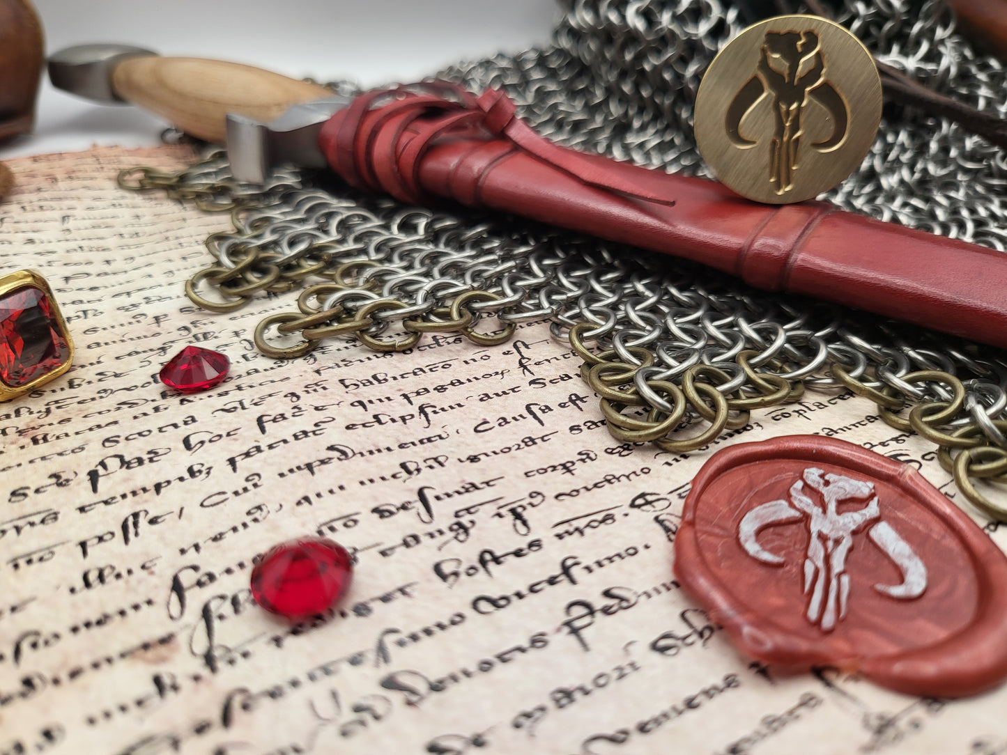 A styled flat-lay of fantasy-themed accessories, including a red wax seal with a silver emblem, a gold key, and a red gemstone, arranged on an antique manuscript with chainmail.