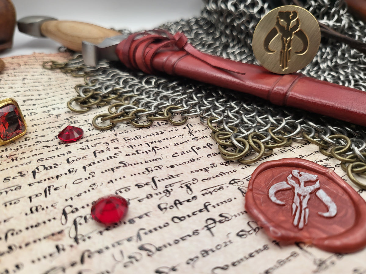 A styled flat-lay of fantasy-themed accessories, including a red wax seal with a silver emblem, a gold key, and a red gemstone, arranged on an antique manuscript with chainmail.