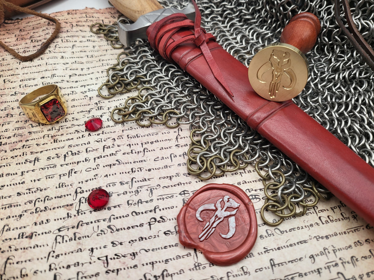 A styled flat-lay of a red leather seal wax stamp set, featuring a red wax seal with a silver key motif, a matching red wax seal on a wooden handle, a gold seal stamp, a gold signet ring, all arranged on a background of chainmail and vintage handwritten manuscript paper.