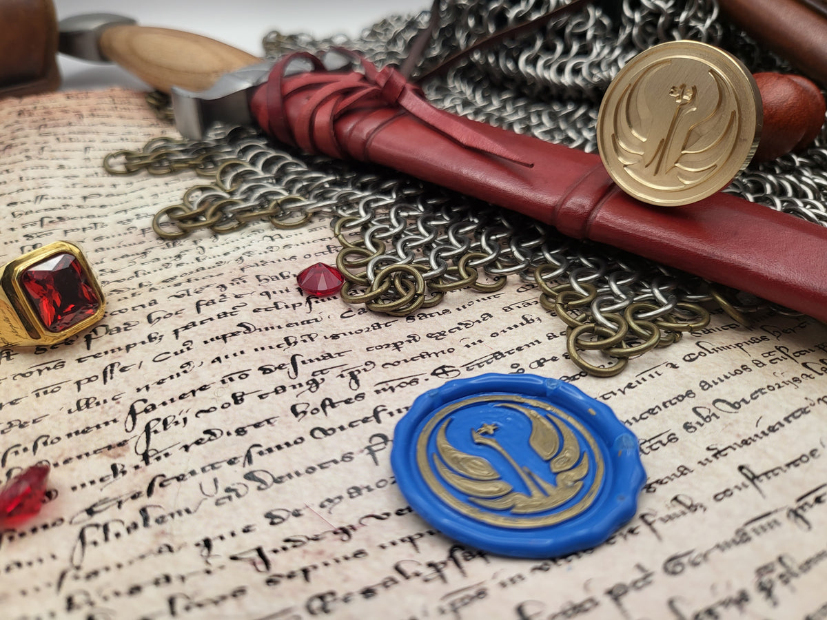 A styled flat-lay of medieval-themed accessories on aged script paper, including a red leather-wrapped quill with a gold emblem seal, a blue wax seal with a gold emblem, chainmail, a red gem ring, and a wooden object.