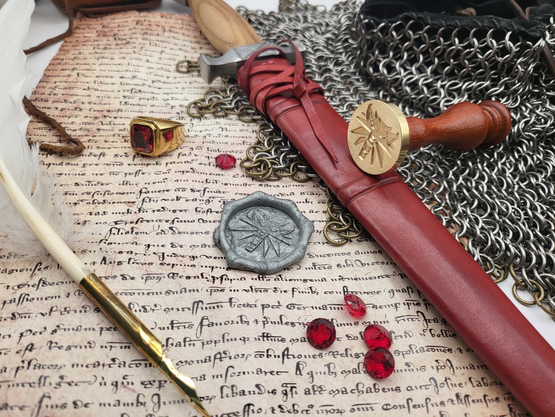 A styled flat-lay of a medieval-themed dagger in a reddish-brown leather sheath, arranged on aged parchment with a wax seal, chainmail, a ring, a quill, and red gem accents.